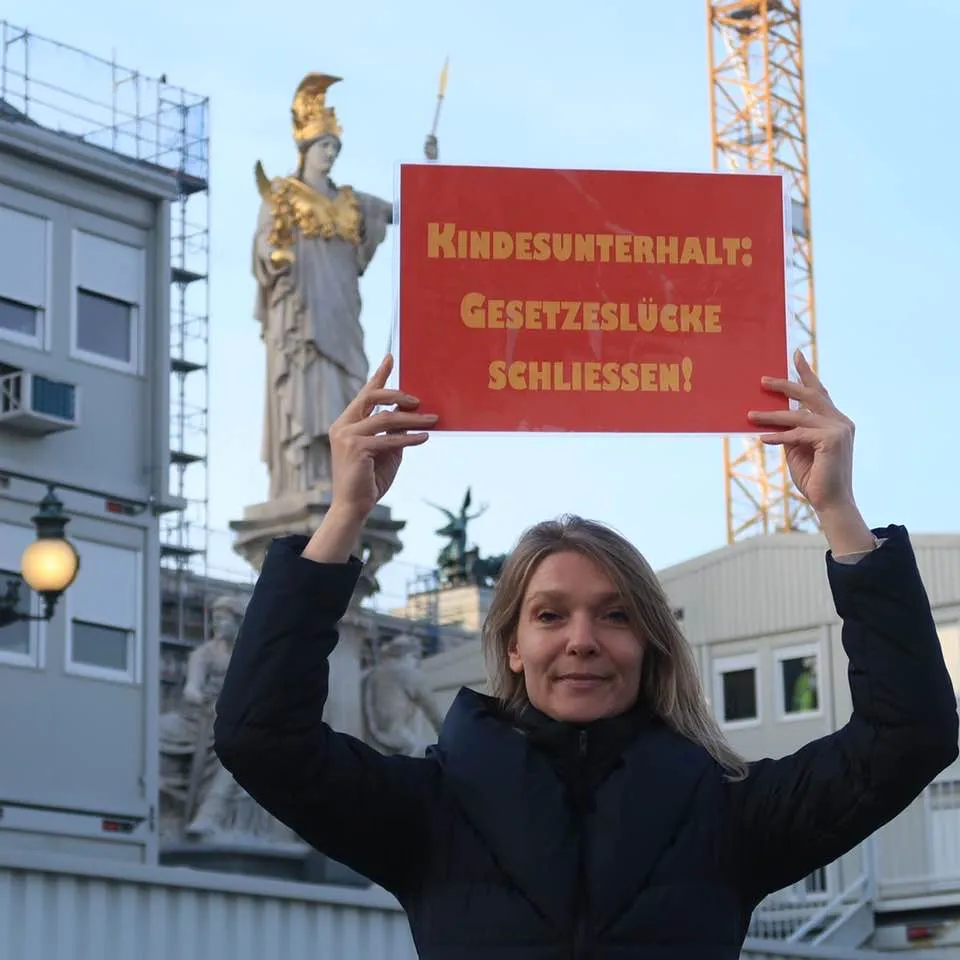 Maria Stern hält ihr rotes Schild „Kindesunterhalt: Gesetzeslücke schließen!“ vor der Pallas-Athene-Statue am Parlament