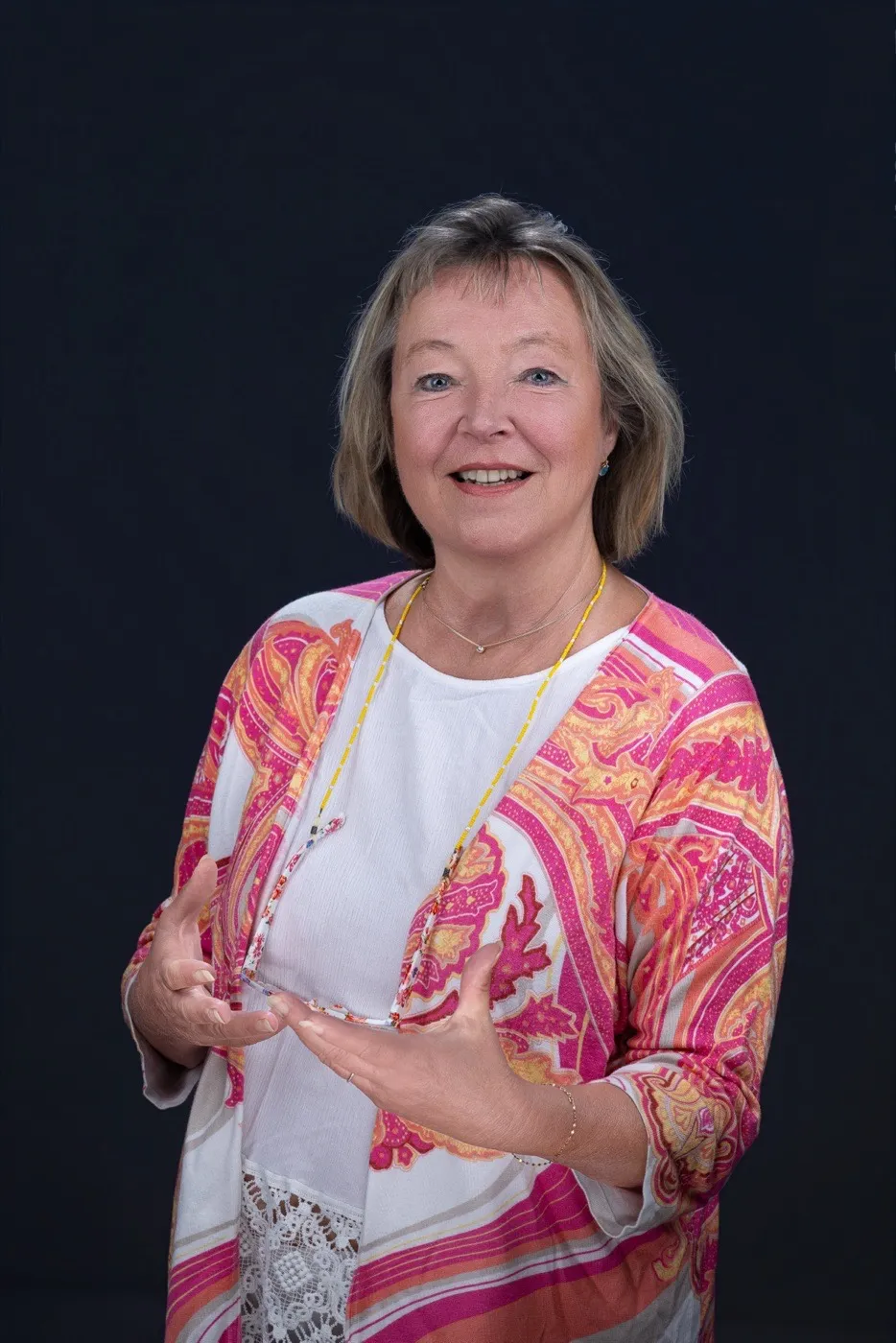 Andrea Einzinger in pink-orange gemusterter Bluse vor dunkelblauem Hintergrund