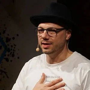Philipp Nägele mit Hut, Brille und Headset-Mikrofon auf einer Bühne