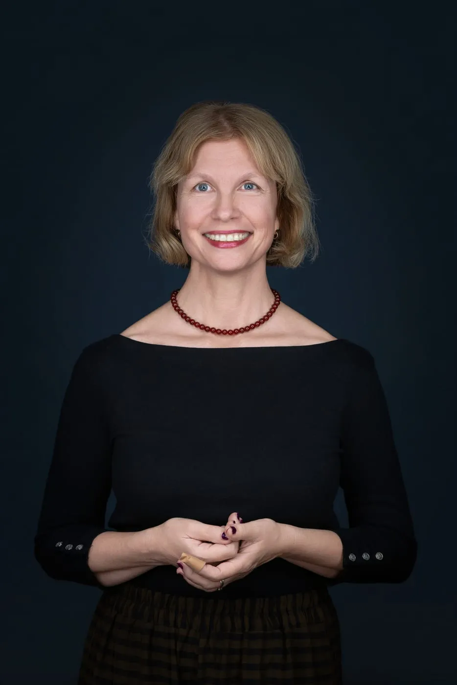 Anke Pfeiffer in schwarzem Oberteil mit roter Kette vor dunkelblauem Hintergrund