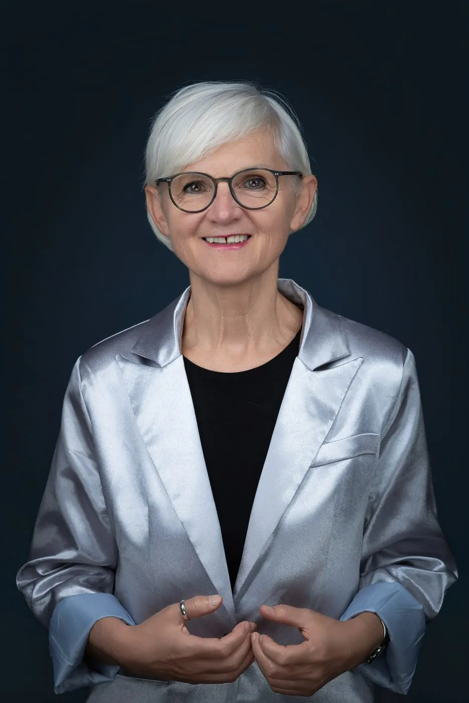 Maria Rösslhumer in silbernem Blazer vor dunkelblauem Hintergrund